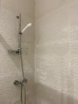Detail of the shower mixer with handheld showerhead and wire soap basket on beige tiled walls